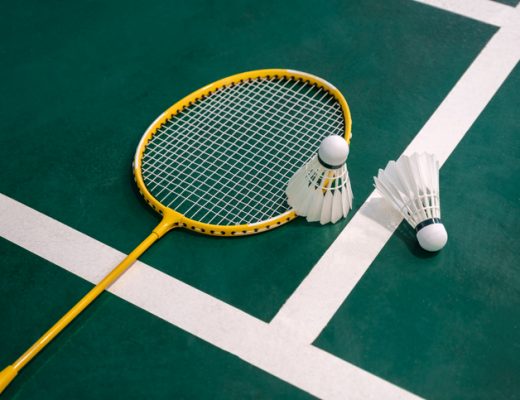 A close up of a yellow badminton racquet and white shuttlecock against a green indoor court