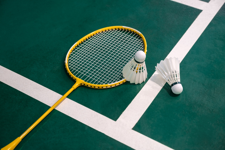 A close up of a yellow badminton racquet and white shuttlecock against a green indoor court