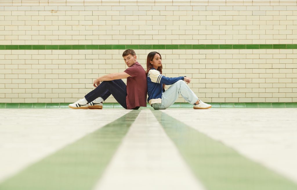 A young man and woman sit back to back in a sports hall
