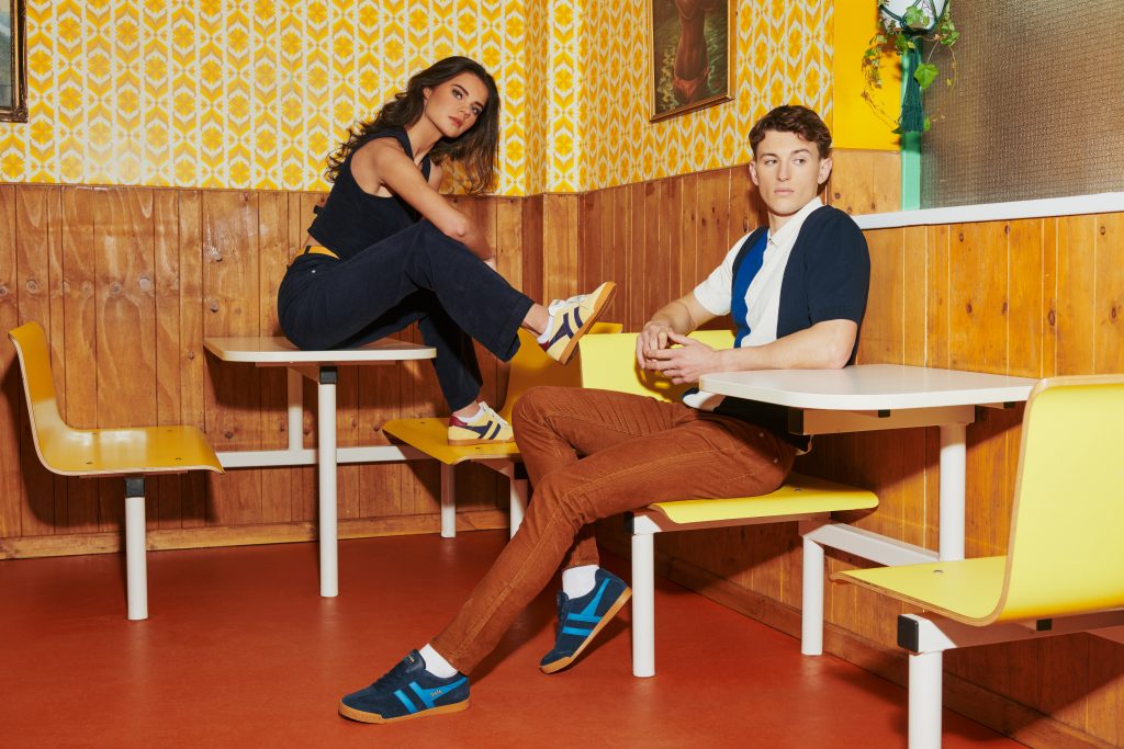 Gola imagery, a man and woman wear Harrier and Elan trainers with terrace fashion in a retro dining area