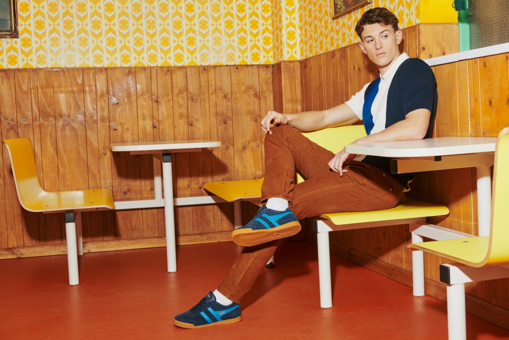 Man wears fitted polo and cords with navy and blue Harrier trainers