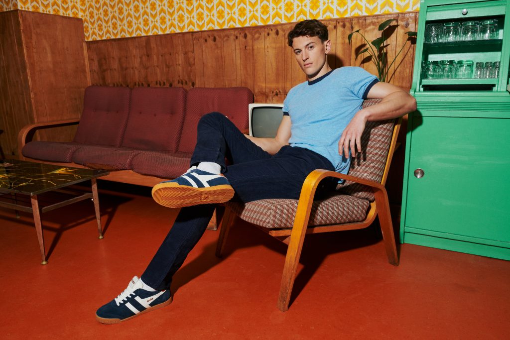 Man wears relaxed casual clothing and navy and white Elan trainers