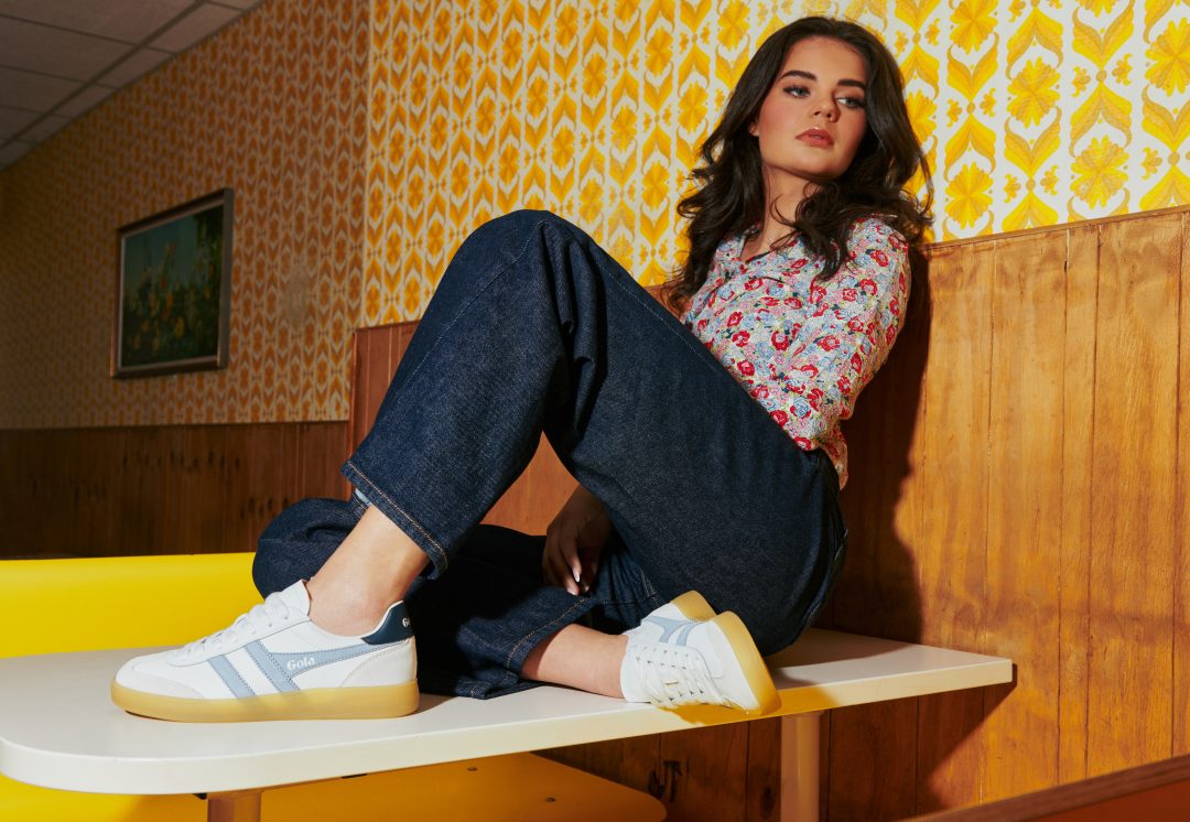 A women sits on a diner table wearing dark denim jeans and Gola Viper trainers