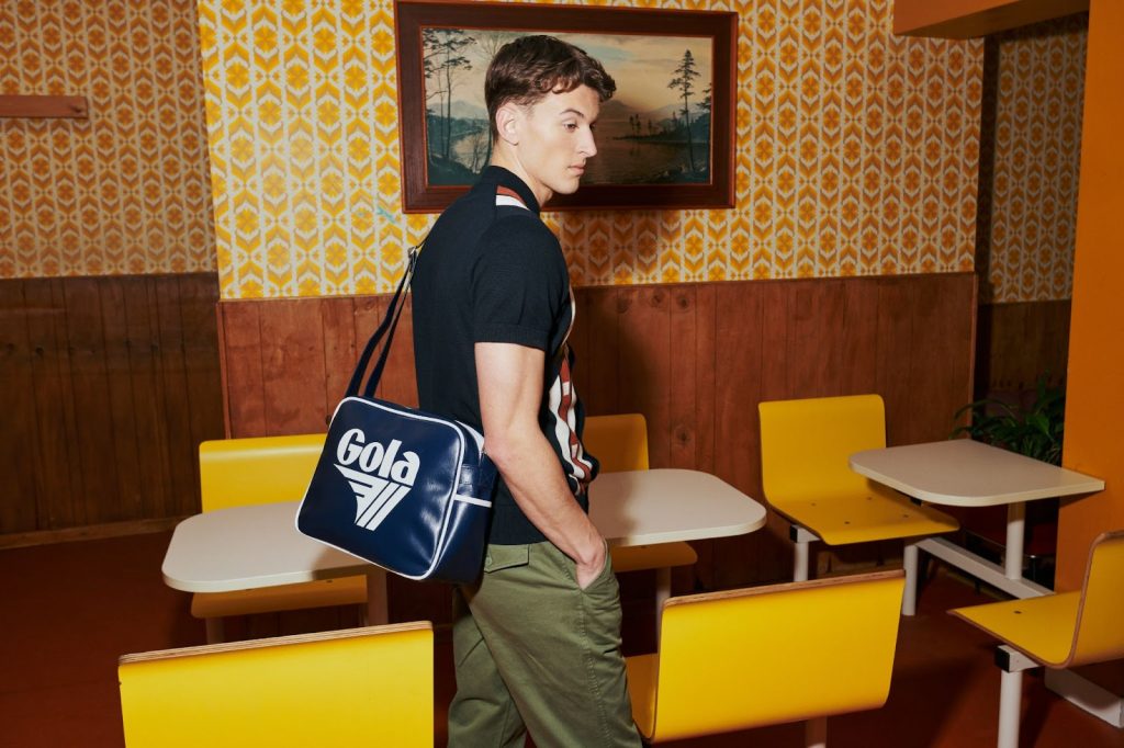 Young man stands in a retro cafe wearing a Gola Redford bag